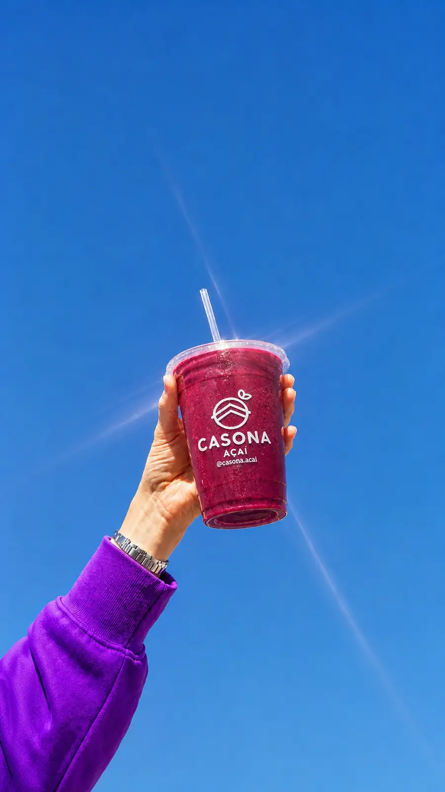 Mão erguendo um copo de açaí Casona contra o céu